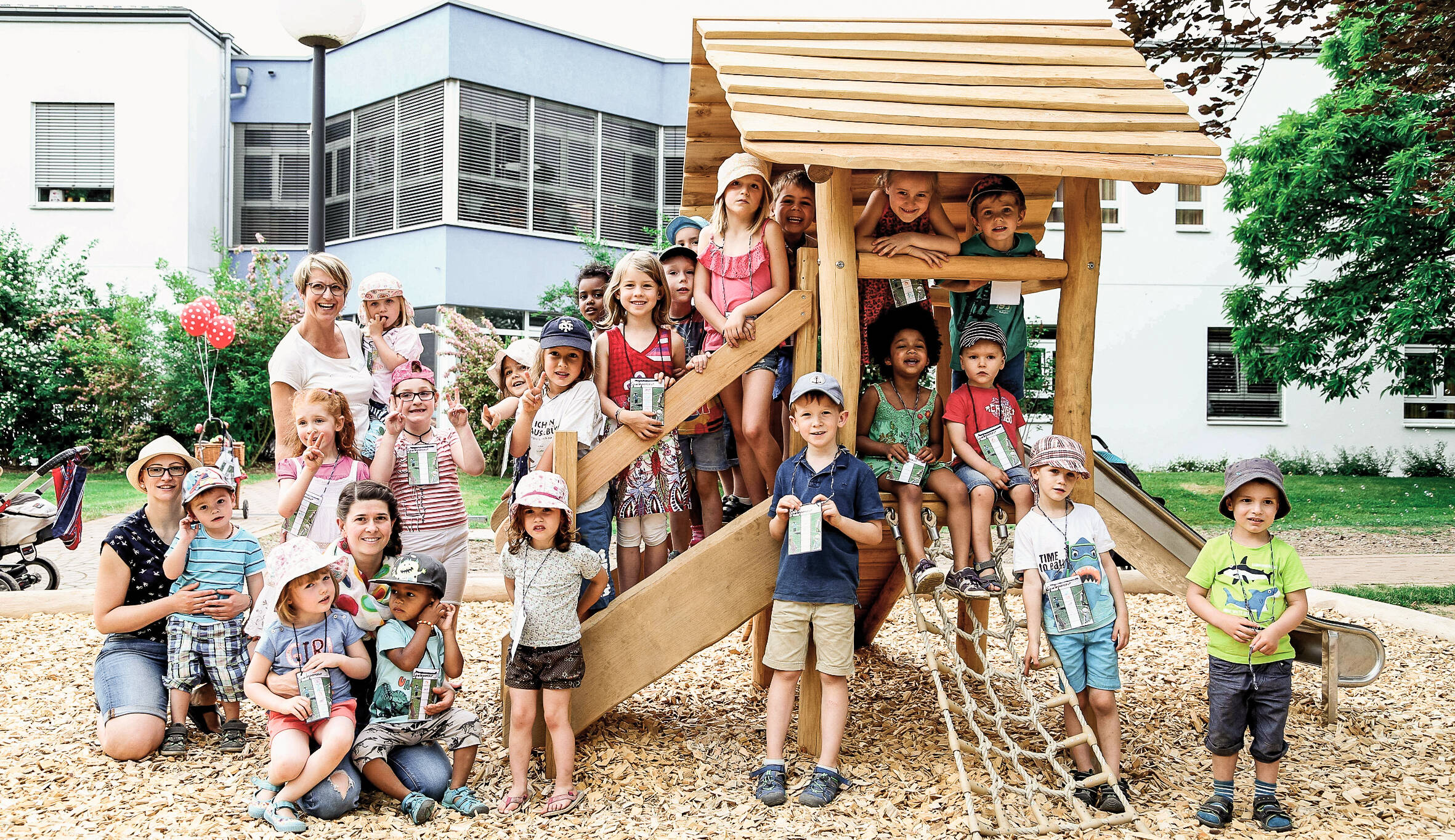 Gruppe von Kindergartenkindern auf und um ein kleines Holzhaus auf einem Spielplatz