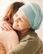 Person mit hellgrüner Kopfbedeckung umarmt lachen eine andere Person