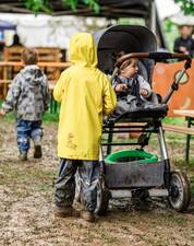 Zwei Kinder im Schlamm in wasserfesten Kleidern und einem Kinderwagen mit einem Kleinkind
