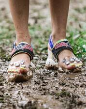 Füße mit bunt lackierten Zehnägeln in bunten Sandalen im Matsch stehend