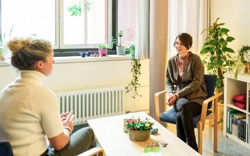 Krebsberatungszimmer: Helles Zimmer mit zwei sitzenden Personen an einem Tisch und vielen Zimmerpflanzen