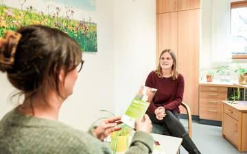 Beratungszimmer mit einem Blumenbild an der Wand rechts und zwei Frauen
