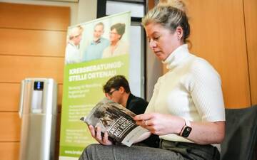 Wartebereich mit zwei Wartenden und einem Roll-Up im Hintergrund der Krebsberatungsstelle Ortenau