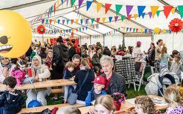 Blick in ein großes Zelt mit bunten Wimpeln an der Decke und vielen Kindern mit ihren Eltern