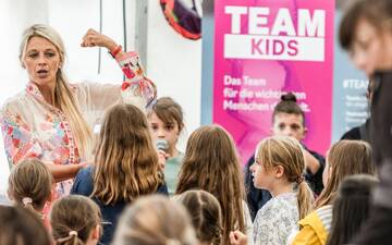 Eine Frau spannt den Arm an, vor ihr eine Gruppe Kinder